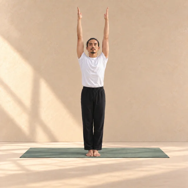 Urdhva Hastasana : modèle debout sur un tapis sauge, les bras tendus au-dessus de la tête dans un studio beige.