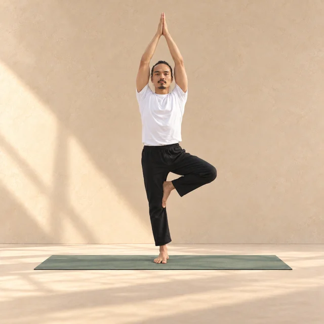Vrksasana : modèle de face en équilibre sur un pied, autre pied posé contre l’intérieur de la jambe et bras levés, sur un tapis sauge en studio.