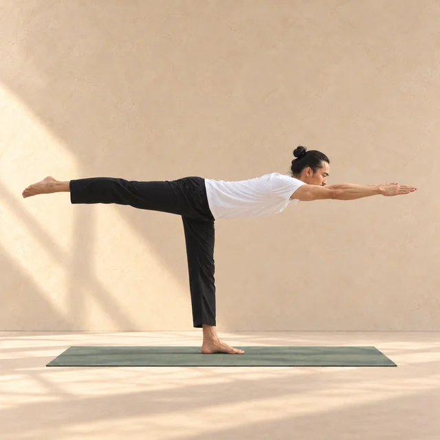 Virabhadrasana III : modèle en équilibre sur une jambe, buste et jambe arrière allongés presque à l’horizontale, bras étendus devant lui au-dessus du tapis sauge.