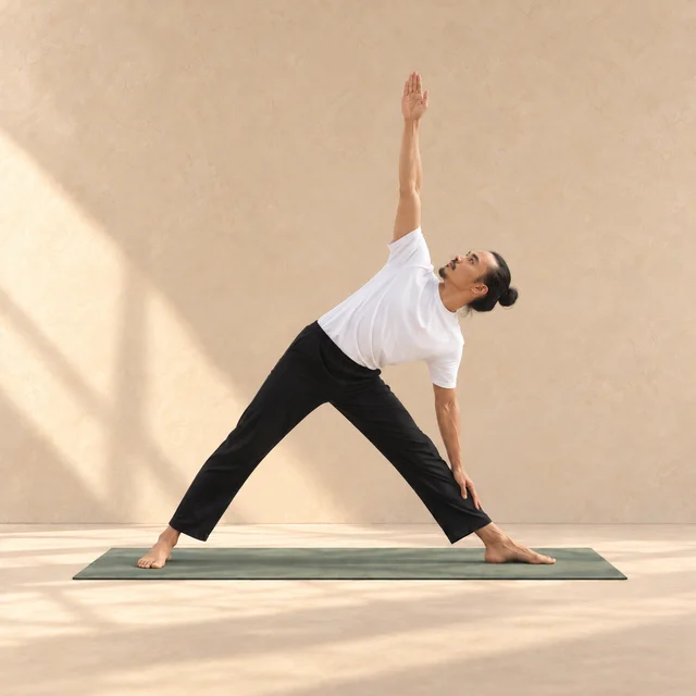 Utthita Trikonasana : modèle jambes écartées, buste incliné au-dessus de la jambe avant, main sur le tibia et bras opposé levé, sur tapis sauge.