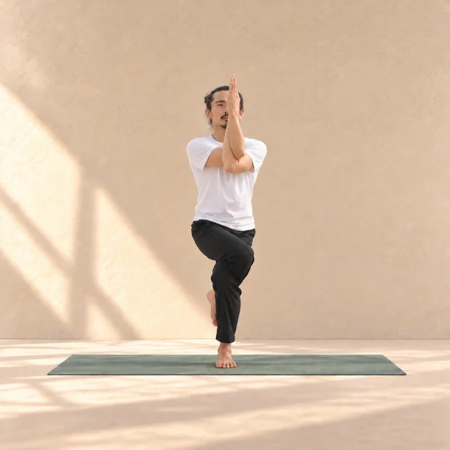 Garudasana de face : cuisse droite visiblement croisée au-dessus de la gauche, pied enroulé derrière le mollet et bras d’aigle devant le visage.