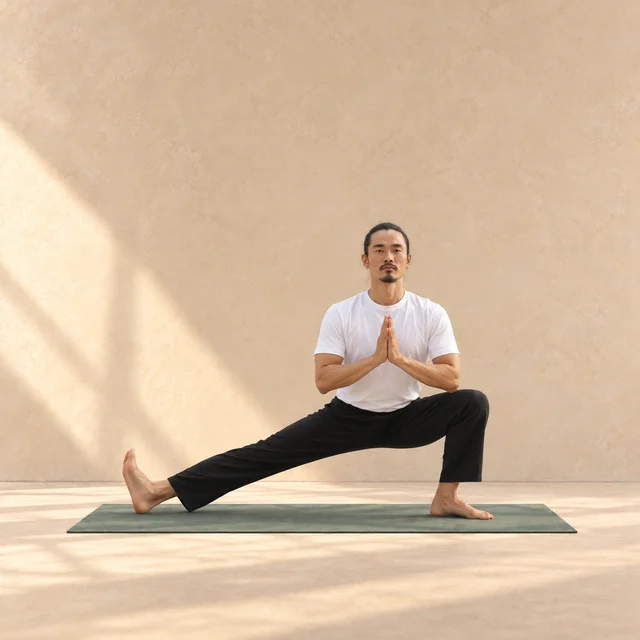 Skandasana de face : jambe droite de l’image fléchie en fente latérale, jambe opposée tendue avec orteils relevés et mains jointes au cœur.