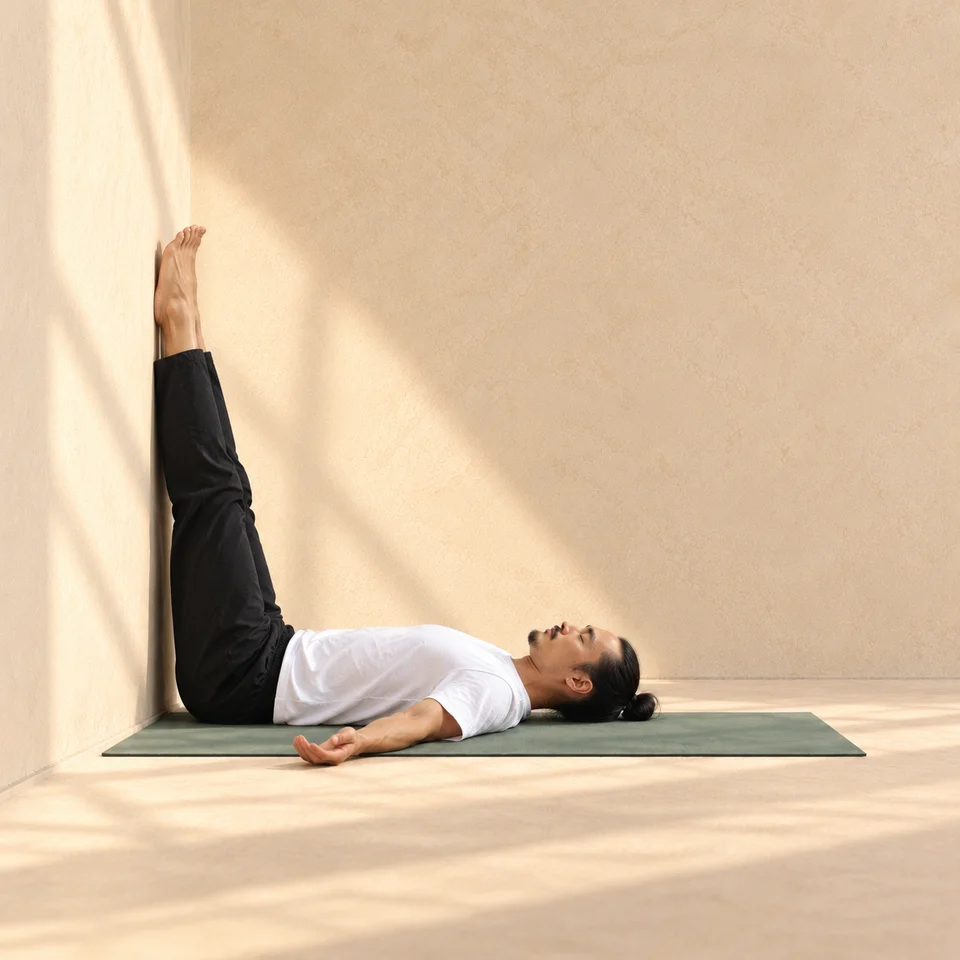 Jambes au mur de profil, tête vers la droite : dos et bassin posés sur le tapis, jambes verticales contre la paroi et bras détendus.