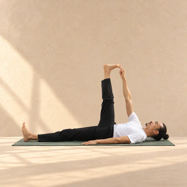 Supta Padangusthasana de profil, tête à droite : dos au sol, jambe gauche allongée, jambe droite presque verticale et gros orteil droit tenu par la main droite.